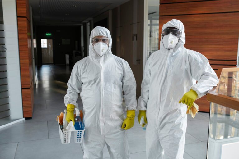 People wearing hazmat suits cleaning and disinfecting an area — representing DIY pest control versus professional services.